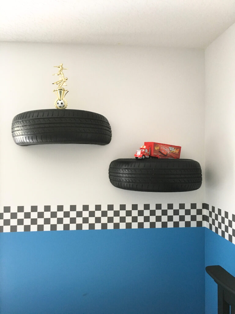 Upcycled golf cart tire transformed into a stylish black shelf, mounted on a wall with L-brackets, adding a creative touch to a race car-themed room.